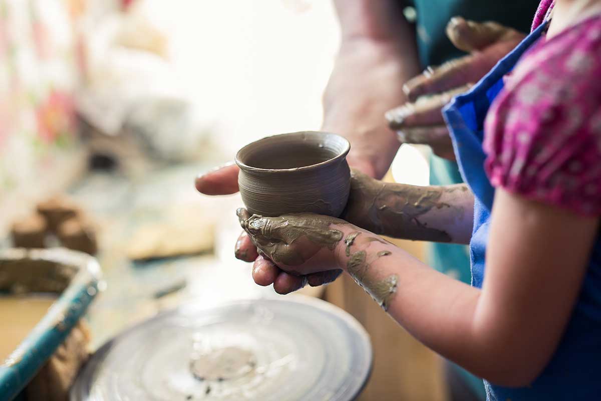 Person holding pot spun on pottery wheel